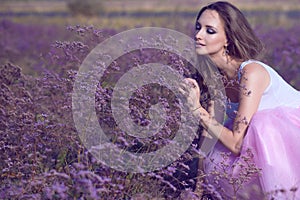 Young chic woman with artistic make up and long flying hair smelling violet flowers with closed eyes