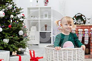 A young child with blonde hair plays by the Christmas tree