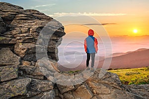 Young child boy hiker standing in mountains enjoying view of amazing mountain landscape at sunrise