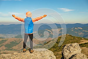 Young child boy hiker standing with raised hands in mountains enjoying view of amazing mountain landscape at sunset