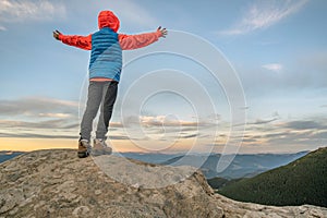 Young child boy hiker standing with raised hands in mountains enjoying view of amazing mountain landscape at sunset