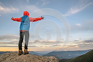 Young child boy hiker standing with raised hands in mountains enjoying view of amazing mountain landscape at sunset