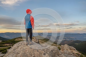 Young child boy hiker standing with raised hands in mountains enjoying view of amazing mountain landscape at sunset