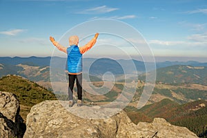 Young child boy hiker standing with raised hands in mountains enjoying view of amazing mountain landscape at sunset