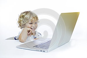 A young child with cheerful expression between 4 and 5 years old sitting at a desk while using a computer