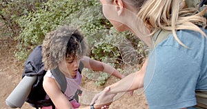 A young child with curly hair receives help from a woman outdoors