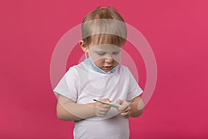 A young child doctor with a medical mask holds a thermometer in his hands and looks at the temperature