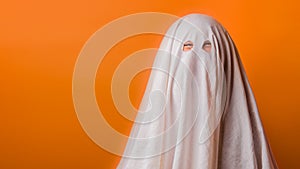 Young child dressed in a ghost costume for halloween on orange background