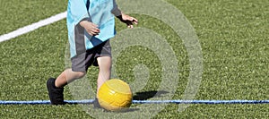 Young child dribbleing a yellow soccer ball on a turf field