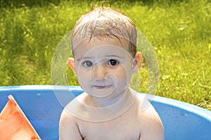 Young child, fun expression, playing with water in a paddling pool.