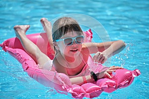 Young child girl falling in water from inflatable air mattress in swimming pool while swinnimg during tropical vacations