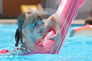 Young child girl falling in water from inflatable air mattress in swimming pool while swinnimg during tropical vacations