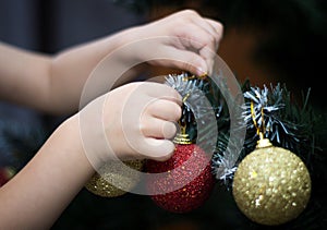 A young child hanging New Year`s toys on the Christmas tree, the child`s hands, close-up, Christmas balls, holiday, arms