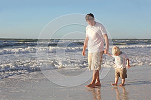 Young Child Holding Father's Hand While Walking in Ocean on Beach