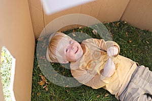 Young Child Laying in Grass while Playing in Cardboard Box Fort