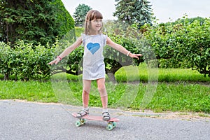 A young child learns to ride a skateboard. Cute little girl is riding on a blackboard in a park