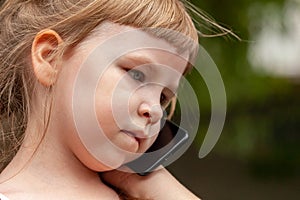 Young child, little girl deep in thought talking on the mobile phone, smartphone. Natural portrait, neutral expression, face