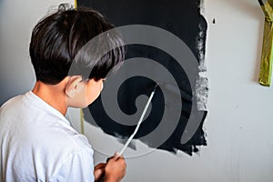 Young child painting a wall in black colour. view from behind