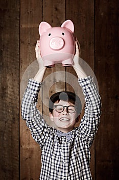 Young child, piggy bank and happy in portrait in studio, money saving and cash savings in youth with retro fashion. Boy