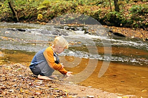 Young Child Playing in River Near Waterfall in Forest