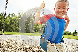 Young child, portrait and smile with swing, park and nature for outdoor fun and play with fresh air. Boy, tree and