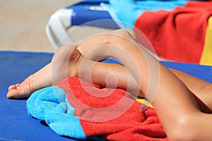 Young child's legs and bright colored towels on a sun lounger in sunshine