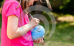 Young child, sa little girl drawing a happy smiling face on a ballon using a black marker outdoors, closeup