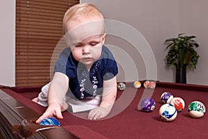 Young child sitting on a billiard table dropping a ball in a pocket