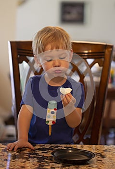 Young child sitting at a table eating a marshmallow