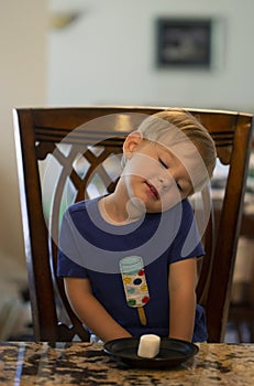 Young child sitting at a table waiting patiently for a marshmallow