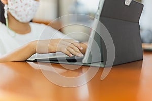 Young child student with protective mask hands typing on laptop.