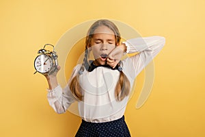 Young child student with ringing alarm clock is lazy going to school. Yellow background