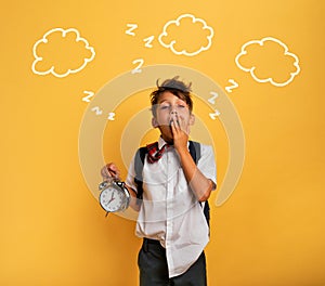 Young child student with ringing alarm clock is lazy going to school. Yellow background.