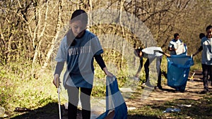 Young child using tongs tool to grab and pick up trash from the woods