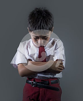 Young child in school uniform feeling sad and depressed looking down scared and embarrassed victim of bullying and abuse