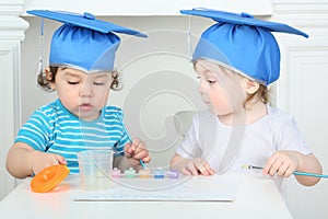 Young children in blue graduation hats paint