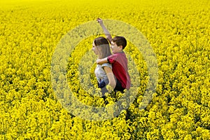 Young children, older sister and younger brother enjoy yellow flowery spring meadow together.