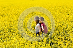 Young children, older sister and younger brother enjoy yellow flowery spring meadow together.