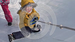 Young children play and have fun on the ice in the winter park. Children pull a rope on the playground of the ice park