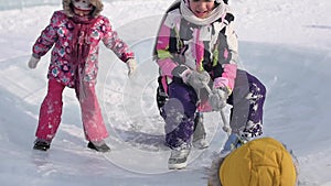 Young children play and have fun on the ice in the winter park. Children pull a rope on the playground of the ice park