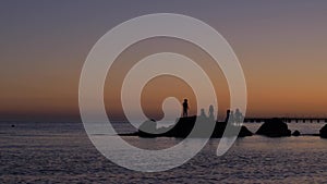 Young children play on the rocks on the beach by the sea at sunset. Silhouettes of children playing on the rocks by the