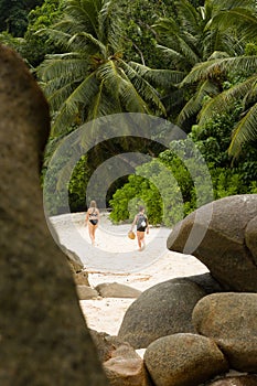 Young children walk together under palm trees, at tropcial sandy beach behind huge rocks photo