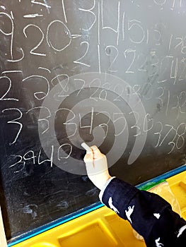 Young childs hand writing numbers on a chalkboard
