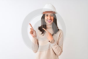 Young chinese architect woman wearing security helmet over isolated white background smiling and looking at the camera pointing