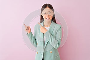 Young chinese businesswoman wearing jacket and glasses over  pink background smiling and looking at the camera pointing