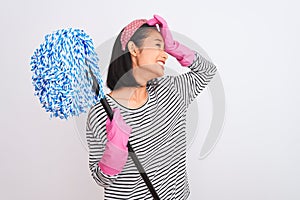 Young chinese cleaner woman wearing gloves holding mop over isolated white background stressed with hand on head, shocked with