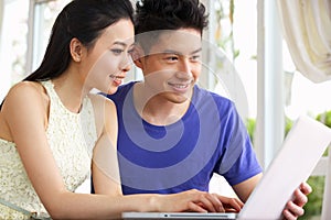 Young Chinese Couple Sitting Using Laptop At Home