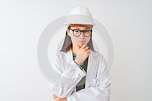 Young chinese engineer woman wearing coat helmet glasses over isolated white background looking confident at the camera with smile