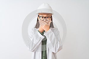 Young chinese engineer woman wearing coat helmet glasses over isolated white background shocked covering mouth with hands for