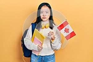 Young chinese girl exchange student holding canada flag depressed and worry for distress, crying angry and afraid